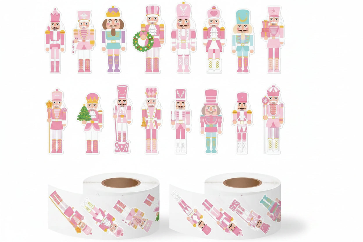 A set of die-cut stickers shaped like pink and multicoloured nutcracker soldiers, shown both as individual cutouts and on rolls. The figures feature various outfits in pink, blue, green, and yellow, with one holding a green wreath and another holding a small Christmas tree.